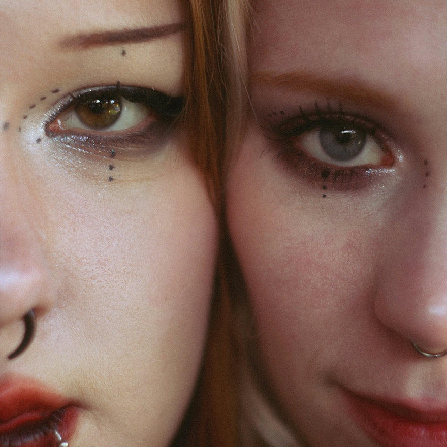 Two women with elaborate makeup and piercings close-up facial features