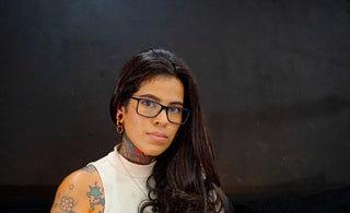 A woman with glasses and tattoos looks forward.