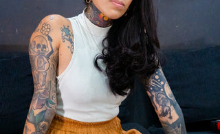 Woman with tattoos and glasses sitting on couch.