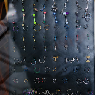 Many colorful body piercings and earrings on a dark display.