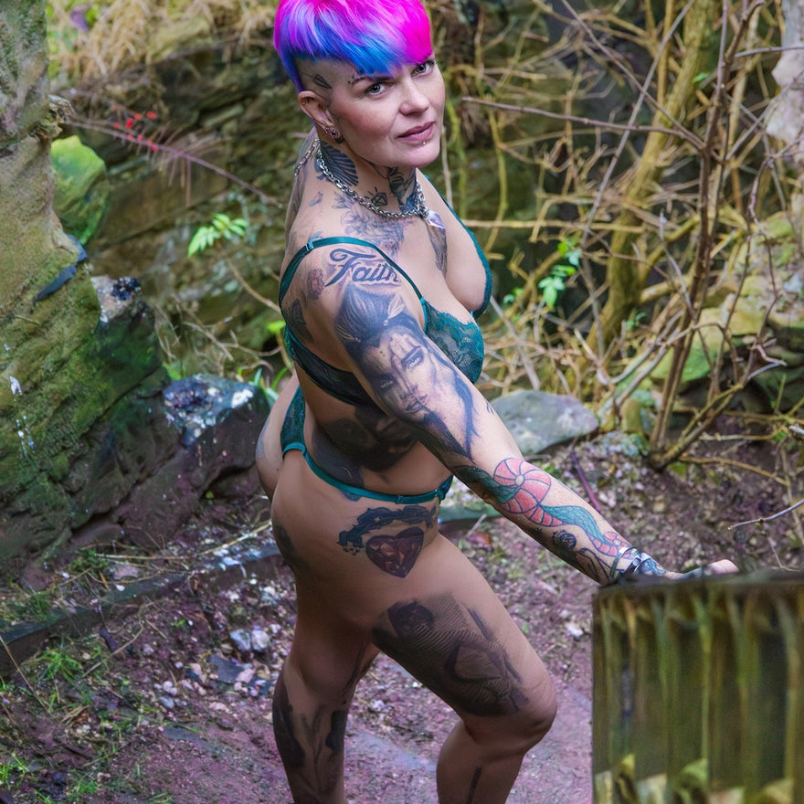 Tattooed woman with vibrant hair stands on an outdoor path